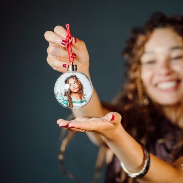 A delighted woman holds up her personalised holiday bauble featuring her own photo inside